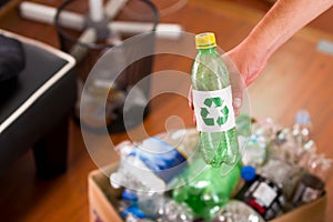 Close up of a hand putting a plastic bottle with a printed sign of recycling in front, inside of a cardboard box full of