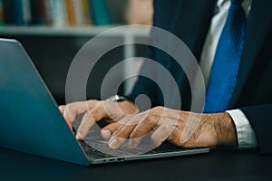 Close up. hand's business man wearing suit typing and working on laptop computer on wooden table at home office.