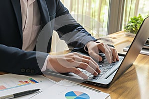 Close up. hand's business man wearing suit typing and working on laptop computer on wooden table at home office.