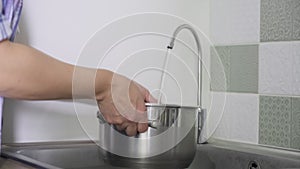 Close-up of hand with saucepan for cooking taking tap purified filtered water
