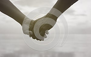 Close up hand of senior couple holding hand together near seaside at the beach,black and white picture color