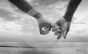 Close up hand of senior couple hook each other's little finger together near seaside at the beach,black and white picture
