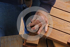 Close up of the hand of a senior man who is using a drill bit to complete a woodworking project to build flooring.