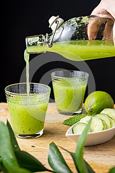 Close-up of hand serving cucumber juice in a glass, lime and green branch out of focus, black phono photo