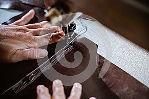 Close up of hand sewing a zipper onto leather