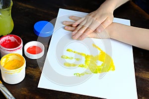 Close-up hand of a small child leaves colored palm prints on white paper, creative creativity concept, fine motor skills, patience