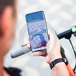 Close up of hand and smartphone, unlocking dockless electric scooter for rent with debranded generic phone app. photo