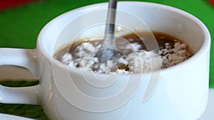 Close-up of Hand stirring sugar in a cup of aromatic coffee with spoon. A cup of aromatic coffee is placed on a wooden table.