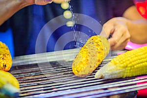 Close up hand of street food vendor while grilling for mixed sweet corn butter. Cook is grilling and sprinkling salt, sugar and b