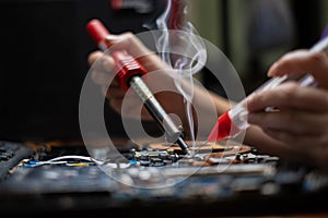 hand technician repairing broken laptop notebook computer with electric soldering Iron photo