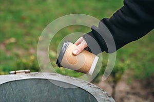 A man throws a paper disposable cup into the trash can in the park.