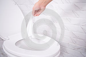 Close up hand throwing toilet paper to the toilet in a white tile bathroom