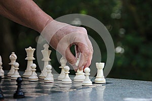 a Close-up of a hand about to move the knight in chess outside in the garden on a stone chess table