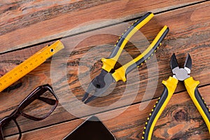 Close-up hand tools include ruler, pliers on brown wooden desk.