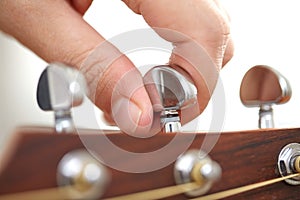 close up of hand tuning guitar strings with pegs