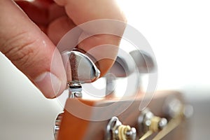 close up of hand tuning guitar strings with pegs