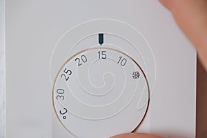 Close-up of hand turns down the temperature to 15 degrees Celsius on an electronic thermostat. Saving energy and money