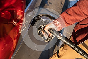 Close up on hand of unknown caucasian man hold black gas pump nozzle pouring gasoline into the fuel tank refueling petroleum to