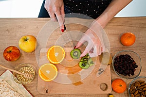 Close up on hand of unknown caucasian woman holding knife cutting kiwi and oranges top view copy space