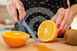 Close up on hand of unknown caucasian woman holding knife cutting oranges copy space
