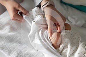 Close up on hand of unknown woman holding leg of her newborn baby - caucasian mother dressing or undressing her little baby on the