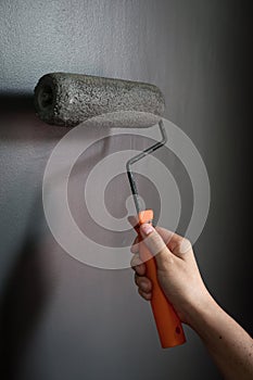 Close up of hand using paint roller applying grey paint on wall.