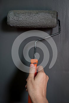 Close up of hand using paint roller applying grey paint on wall.