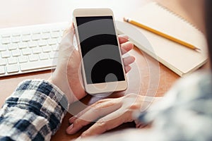 Close up hand using smartphone on desk background in office.  On hand holding smartphone blank display