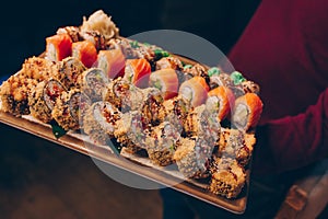 Close-up Hand Waiter holding Set Delicious fresh Sushi slate plate, Japanese raw fish Warm Ebi Sake Unagi . Philadelphia flesh