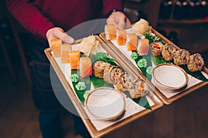 Close-up Hand Waiter holding Set Delicious fresh Sushi slate plate, Japanese raw fish Warm Ebi Sake Unagi . Philadelphia flesh