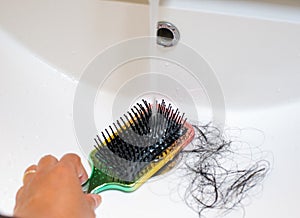 Close-up a hand washing hairbush with Pile of hair loss in bathroom after wash hair.