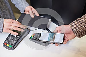 A close-up hand which is holding a smartphone while paying using NFC in a store