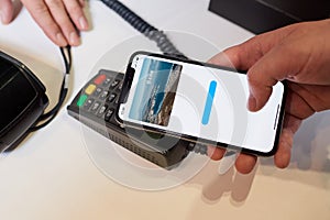 A close-up hand which is holding a smartphone while paying using NFC in a store