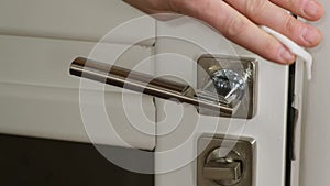 A close up of a hand wipes a door handle with wet napkin. Close up.
