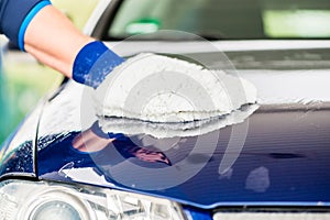 Close-up of hand wiping car with microfiber wash mitt photo