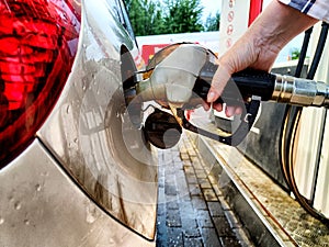 Close up of hand of woman holding gas gun while refueling car with gasoline. Filling fuel into tank of auto at gas