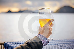 Close up hand of a woman holding a glass of beer with blurred sea, sky and island background