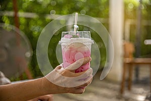 Close up hand of woman holding strawberry smoothie in plastic cup. over nature background