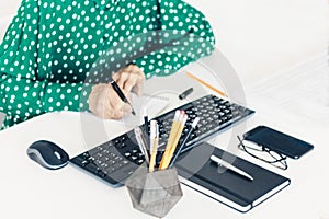 Close-up of hand woman makes notes and using a mouse and typing on keyboard on white table, business concept