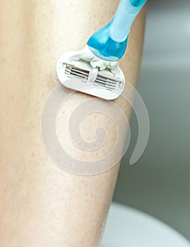 Close up of hand woman shaves leg disposable razor. Moistening and hair removal concept