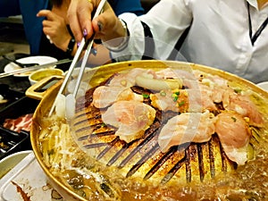 Close up hand of woman using chopsticks eating grill raw sliced beef and pork on the hot golden stainless steel stove