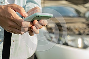 Close up hand of woman using smartphone and blur of her broken car parking on the road. Contacting car technician or