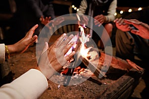 Close-up on hand of woman warming on campfire. Group of asian friends sitting around campfire in the night.