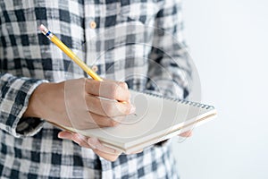 close up on hand writing paper notebook. On young woman left hand holding notebook and right hand writing diary