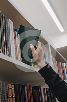 close-up of hand, young adult man stands in library in middle of shelves and takes book. reading and recreation