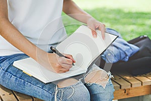 Close-up hand of young female student taking note in to diary book. Selective focus on hand holding a pen