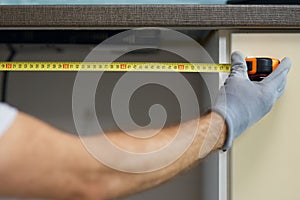 Close up of hand of young repairman, professional plumber using measure tape while doing plumbing work in a new flat