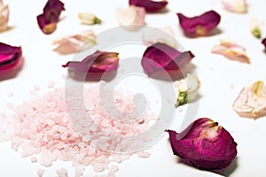 pink himalayan salt crystals surrounded by red rose petals with blur background. Concept of spa treatment with pink salt