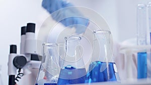 Close up handheld footage of female scientist doing scientific test with blue liquid from test tubes