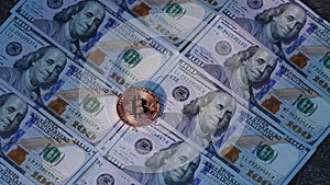 Close-up of a handputs bitcoin on a stack of hundred dollar bills. Money background and golden coin of cryptocurrency.